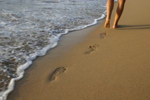 legs walking barefoot in the sand next to the beach shoreline